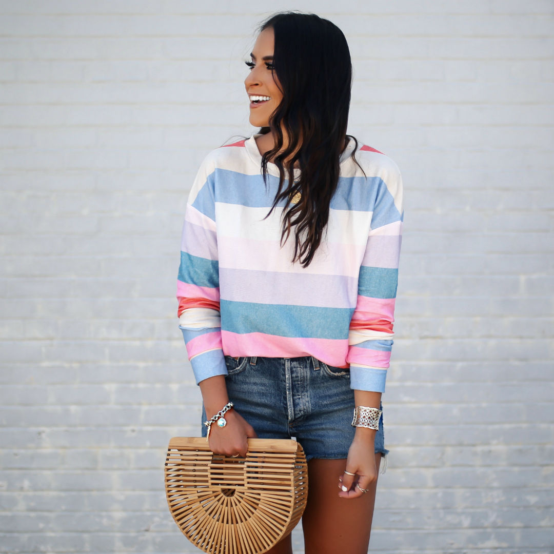 Blogger, Sarah LIndner of The House Of Sequins wearing a rainbow pullover from amazon paired with denim shorts and a summer bag