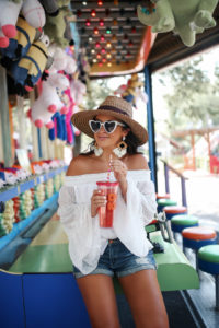 Blogger Sarah Lindner of The House of Sequins wearing white Off Shoulder Tops Polka Dot from amazon prime, BlankNYC shorts, Brixton Joanna Hat. What to wear to an amusement park